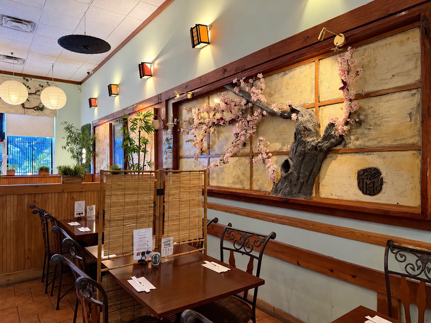 Tables and wood booths beside the cherry-blossom wall at Midori Sushi